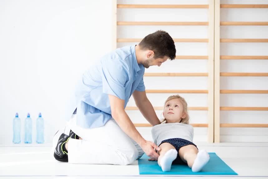 Kinetoterapeut lucrând cu o fetiță pe saltea — exerciții MEDEK