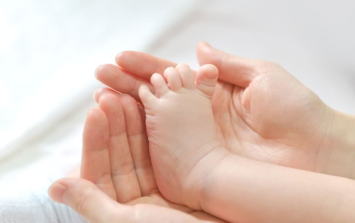 Piciorușul unui bebeluș sprijinit cu grijă în palmele unui adult
